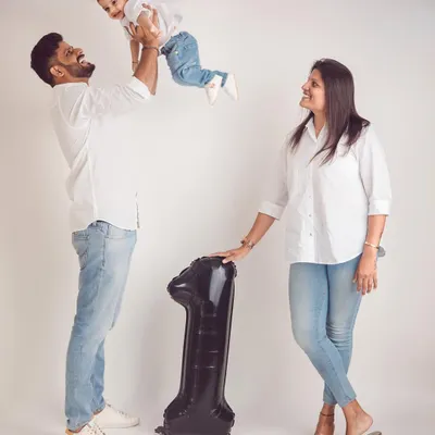 A classic first birthday studio shot. The dad lifting his son in the air captures the pure joy of this milestone, with the number '1' balloon marking the day.