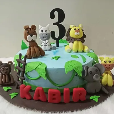 A wild jungle adventure for a third birthday. This cake is decorated with hand-molded fondant animals like a lion, elephant, and monkey, set around a jungle watering hole.