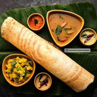 A classic Masala Dosa platter, showcasing the golden-brown crepe with its accompanying potato filling, sambar, and chutneys. Our live dosa station is a centerpiece of interactive culinary entertainment for weddings and parties.
