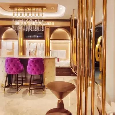 The main counter and seating area at the Sleeep Boutique, designed to feel both exclusive and welcoming. The combination of gold metal screens, a marble counter, and bold fuchsia chairs defines the space's playful opulence.