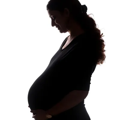 A classic solo maternity silhouette. This timeless image beautifully captures the curve of the baby bump and the mother's gentle, loving expression as she looks down. It's a simple, powerful, and deeply personal portrait.