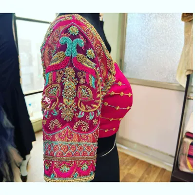A side view of a stunning pink blouse where the entire sleeve is dedicated to a magnificent peacock motif. The vibrant turquoise and gold threads create a truly eye-catching design.