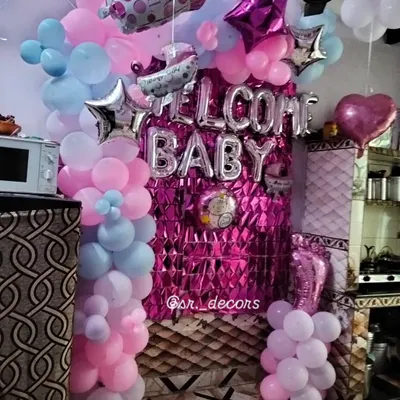 This is a popular and affordable welcome baby setup for your home. It includes a bright pink foil curtain, silver 'WELCOME BABY' balloons, and balloon pillars in a mix of pink, blue, and purple.