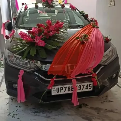 This is an example of a premium wedding car decoration on a Honda City. It features a large arrangement of fresh red flowers on the hood, complemented by pink and red fabric draping for an elegant look.
