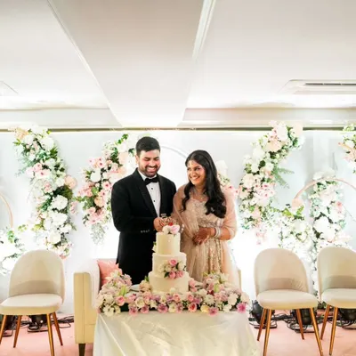 A beautiful moment of a couple cutting their three-tiered wedding cake. Set against a stunning floral backdrop, this cake featured layers of chocolate ganache, praline, and strawberry fresh cream.