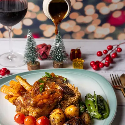 A festive plate of roasted lamb shank with a glass of red wine, set against a backdrop of twinkling Christmas lights.