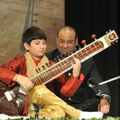 A photo of my father and first guru, Sanjay Rikhiram, introducing me on stage for the first time. My musical journey is rooted in my family's century-long tradition of handcrafting the finest Indian instruments.