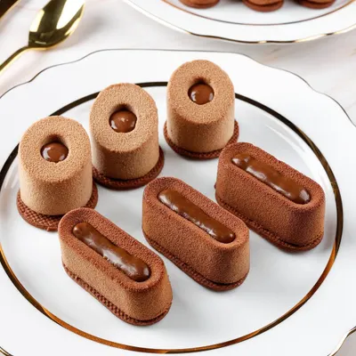 The clean lines and velvety texture of these chocolate entremets are highlighted with precise lighting for a high-end patisserie look.