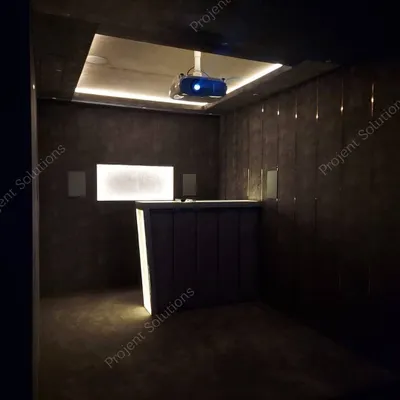 An ambiently lit view of a theater's rear section, highlighting the custom bar, wall-mounted speakers, and the glow from the ceiling-mounted projector.