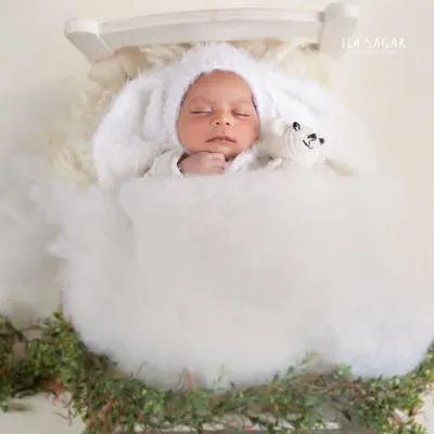 A classic newborn portrait achieved with a miniature white bed, a fluffy cloud like blanket, and an adorable bunny bonnet. These items help create a dreamy, peaceful mood.