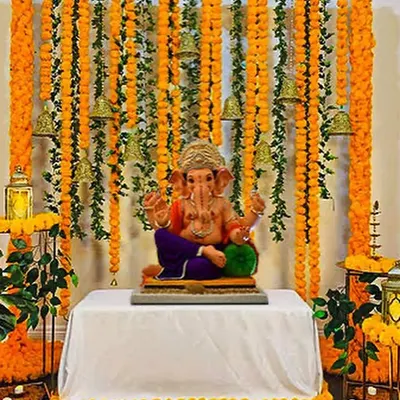 A traditional Ganpati decoration using marigold flower garlands and brass bells to create a beautiful and auspicious backdrop for the idol.