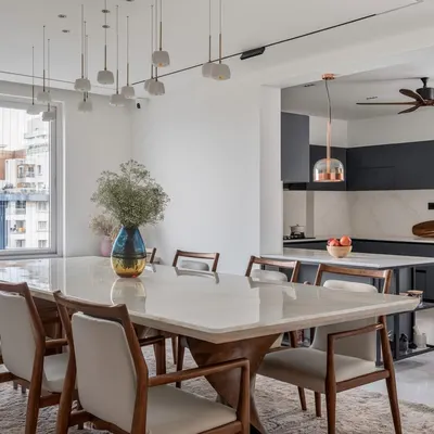 We specialize in creating cohesive, open-plan living areas. This view shows how the elegant dining space, with its onyx tabletop and statement lighting, flows seamlessly into a modern, minimalist kitchen. This approach enhances natural light and creates a perfect environment for family life and entertaining.