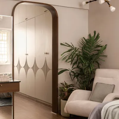 This bedroom corner is a study in calm. A custom wardrobe with a subtle geometric pattern is framed by a dark wood arch, while a comfortable armchair and a large plant create a perfect spot for relaxation.