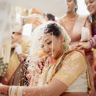A beautiful moment from a South Indian wedding ceremony, where the bride is showered with sanctified rice. The bride's joyful expression is a perfect picture of tradition and happiness.