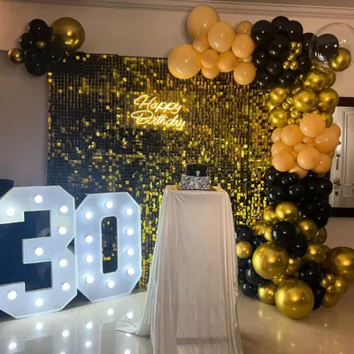 A classic and glamorous 30th birthday celebration. This setup features a gold sequin wall, a black and gold balloon arch, a "Happy Birthday" neon sign, and large light-up numbers for the big 3-0.