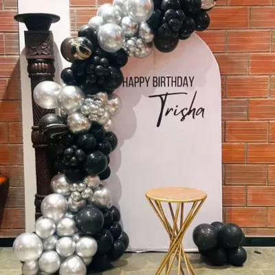 To make the decoration feel more personal, I can add the birthday person's name to the backdrop. Here, the name "Trisha" is featured in a stylish font on a modern, arched panel.