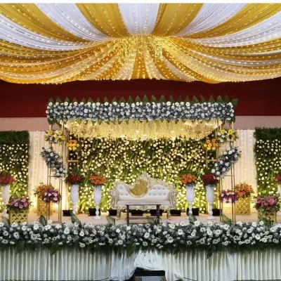 A wide view of a grand reception stage with a full floral backdrop, ceiling drapery, and extensive lighting. This setup is ideal for large convention halls and creates a luxurious atmosphere.