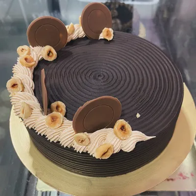 A rich chocolate hazelnut cake. This design features a textured chocolate ganache, hazelnut buttercream, and is topped with toasted hazelnuts and chocolate discs.