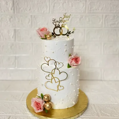 A beautiful two-tier vanilla cake we curated for an engagement ceremony. It's adorned with fresh roses, pearl details, and elegant gold heart accents.