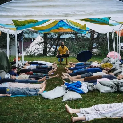 Participants in an outdoor sound bath session rest in Savasana as I facilitate from the front, using various instruments to create a healing soundscape. This shared experience under the open sky connects us to both nature and each other.