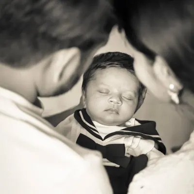 A beautifully composed newborn photo. This close-up, black and white shot shows the parents gazing down at their sleeping baby, creating a frame of love around their new arrival.