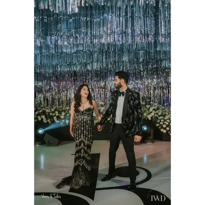 A glamorous couple ready for their cocktail night. Standing beneath a ceiling of shimmering silver tassels, their elegant attire and loving gaze set the tone for an evening of sophisticated celebration and dancing.