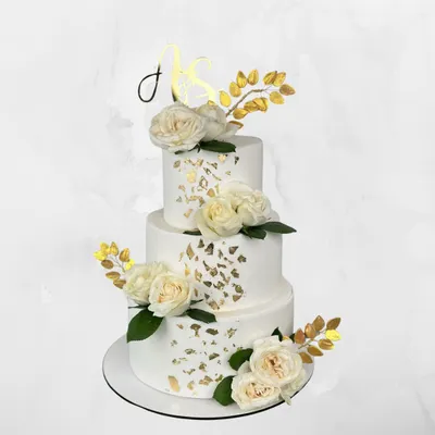 A classic white and gold three-tier wedding cake. The clean lines, delicate gold leaf, and fresh white roses create a look of timeless elegance for your big day.