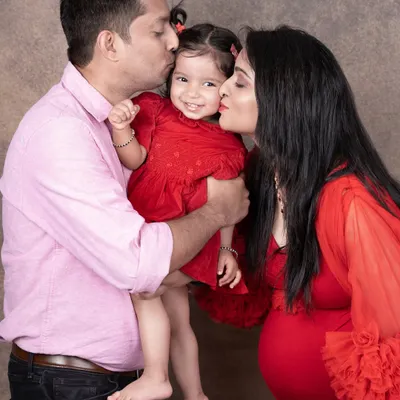 A beautiful family moment during a maternity shoot, with both parents kissing their daughter's cheeks as they await their new arrival.