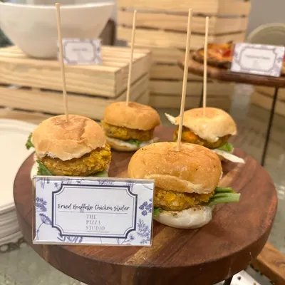 Our popular Fried Truffle Chicken Sliders. These mini burgers are packed with flavor and served on a wooden board, making them a perfect and easy-to-eat option for any party.