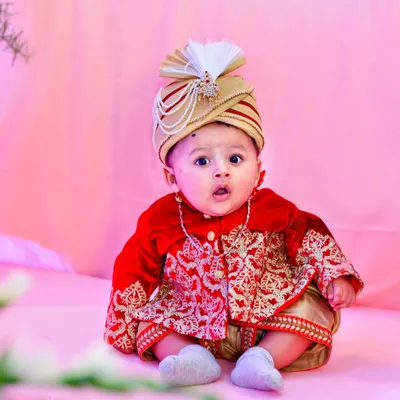 A vibrant, full-color portrait of a baby boy dressed in a traditional red and gold sherwani and turban. This shot highlights our ability to capture sharp, expressive images in themed setups.