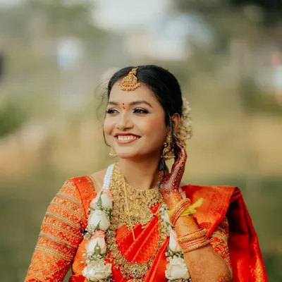 A radiant South Indian bride in her bright orange Kanjeevaram saree, adorned with temple jewelry and a floral garland.
