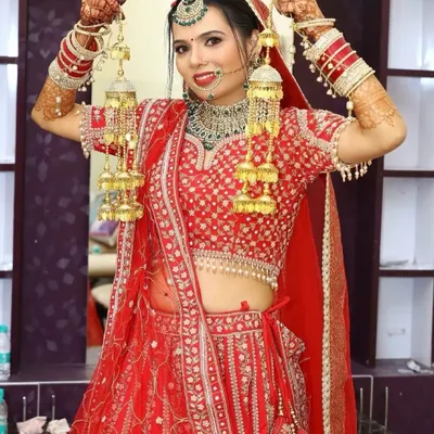 A joyful bride ready for her ceremony. This look features a classic red lip, defined eyes, and a flawless base, perfectly complementing her red lehenga and green Kundan jewellery.