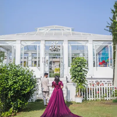 A dramatic and elegant shot from behind, capturing the bride's magnificent flowing gown as the couple walks towards a beautiful white conservatory. A perfect blend of fashion and romance.