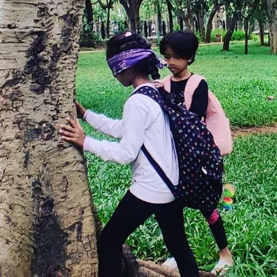 A blindfolded child gently touches the bark of a tree, learning to identify it using her sense of touch. This sensory activity builds a deeper, more intimate connection with trees.