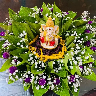 An auspicious tray arrangement perfect for starting any ceremony. A small Ganesha idol sits at the center of neatly arranged betel leaves, accented with baby's breath and purple flowers for a fresh and traditional look.