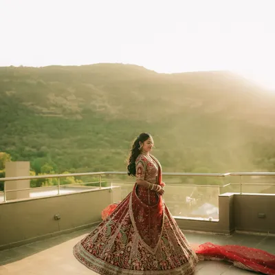 A bride twirls in her magnificent red lehenga on a rooftop at sunset, creating a breathtaking and epic portrait against the mountain landscape.