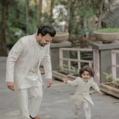 A heartwarming moment captured with a father and son in matching off-white sherwanis. The outfits feature subtle embroidery, creating a classic and elegant coordinated family look.