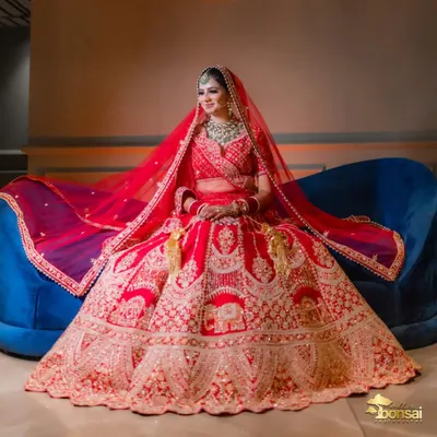 A breathtaking full-length portrait of the bride on a sofa, showcasing her magnificent red lehenga in all its glory. A truly regal bridal shot.