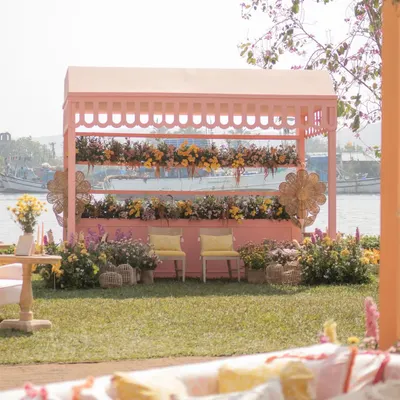 A 'Riverside Brunch' in Goa with a charming pink stall set against the water. The design uses a soft pastel palette and lush florals for a relaxed, garden-party feel.