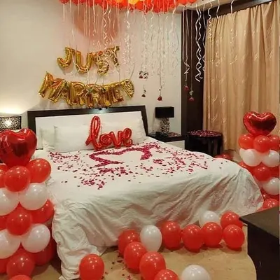The quintessential 'Just Married' room decor. This romantic setup includes balloon columns, a 'love' foil balloon, and a heart shape made from fresh rose petals on the bed.