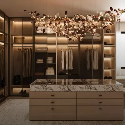A masterpiece of design, this walk-in closet features a marble-topped central island and a stunning chandelier, blending opulent style with practical drawer storage for a truly luxurious feel.