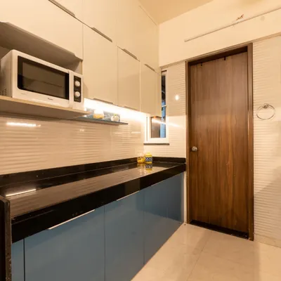 This modular kitchen from a Pune home tour features a beautiful combination of blue and white cabinets, a sleek black countertop, and under-cabinet lighting for a chic and functional space.