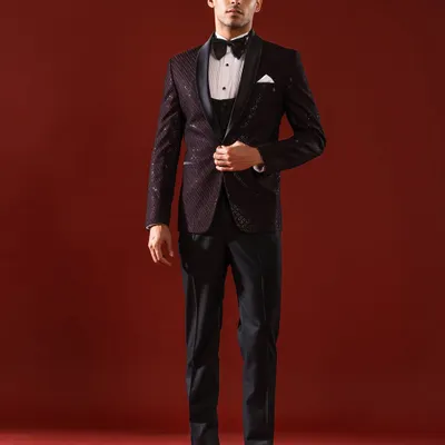 This three-piece tuxedo in a deep burgundy features a subtle, shimmering pattern on the jacket, paired with a classic waistcoat and bow tie. It is an ensemble designed for the gentleman attending a black-tie gala or a formal wedding reception.