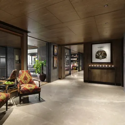 The entrance lobby of the Caitriona apartment in Gurugram, transformed with Sukupira wood veneer, Burberry Beige stone flooring, and olive grey walls. A pair of 'Arizona Armchairs' upholstered in a hand-woven durrie creates a welcoming vignette.