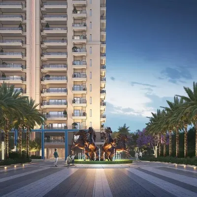 A statement entrance for a housing community in Greater Noida, featuring a grand water fountain with majestic horse sculptures. The wide road, flanked by an avenue of palm trees, creates an unforgettable and grand sense of arrival.