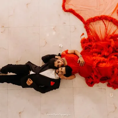An artistic top-down shot of a couple lying on a marble floor. The bride's dramatic red gown flows out, creating a stunning, high-fashion portrait.