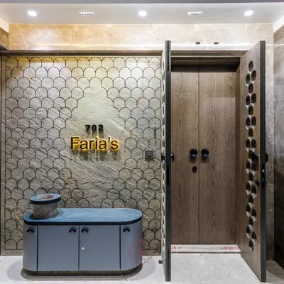 This stunning home entrance features a custom-designed main door with a unique perforated pattern, set against a wall with an intricate fish-scale texture. The wooden inner door adds a layer of warmth and security.