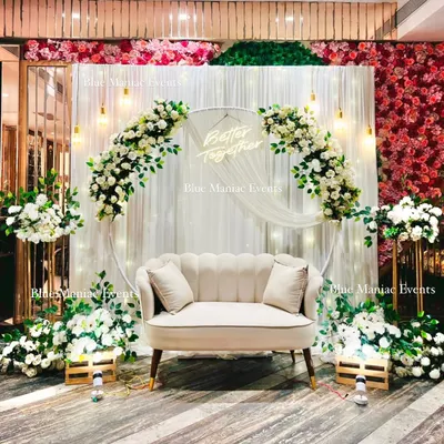 A full view of this beautiful white-themed Roka setup. The design includes a large floral ring, a 'Better Together' neon sign, and additional floral arrangements on stands, creating a complete and immersive photo corner in the venue.