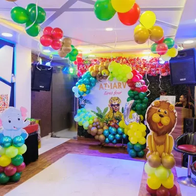 A full view of a fantastic jungle-themed party for a fourth birthday. The setup includes a large balloon arch over a personalized backdrop, cute animal standees like a lion and elephant, and balloon bunches hanging from the ceiling to create a complete jungle canopy effect.