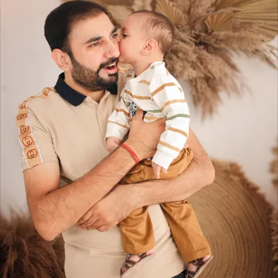 A father receiving a sweet kiss from his son during their boho-themed family photoshoot. The natural, earthy backdrop with pampas grass complements the warmth of this candid moment.